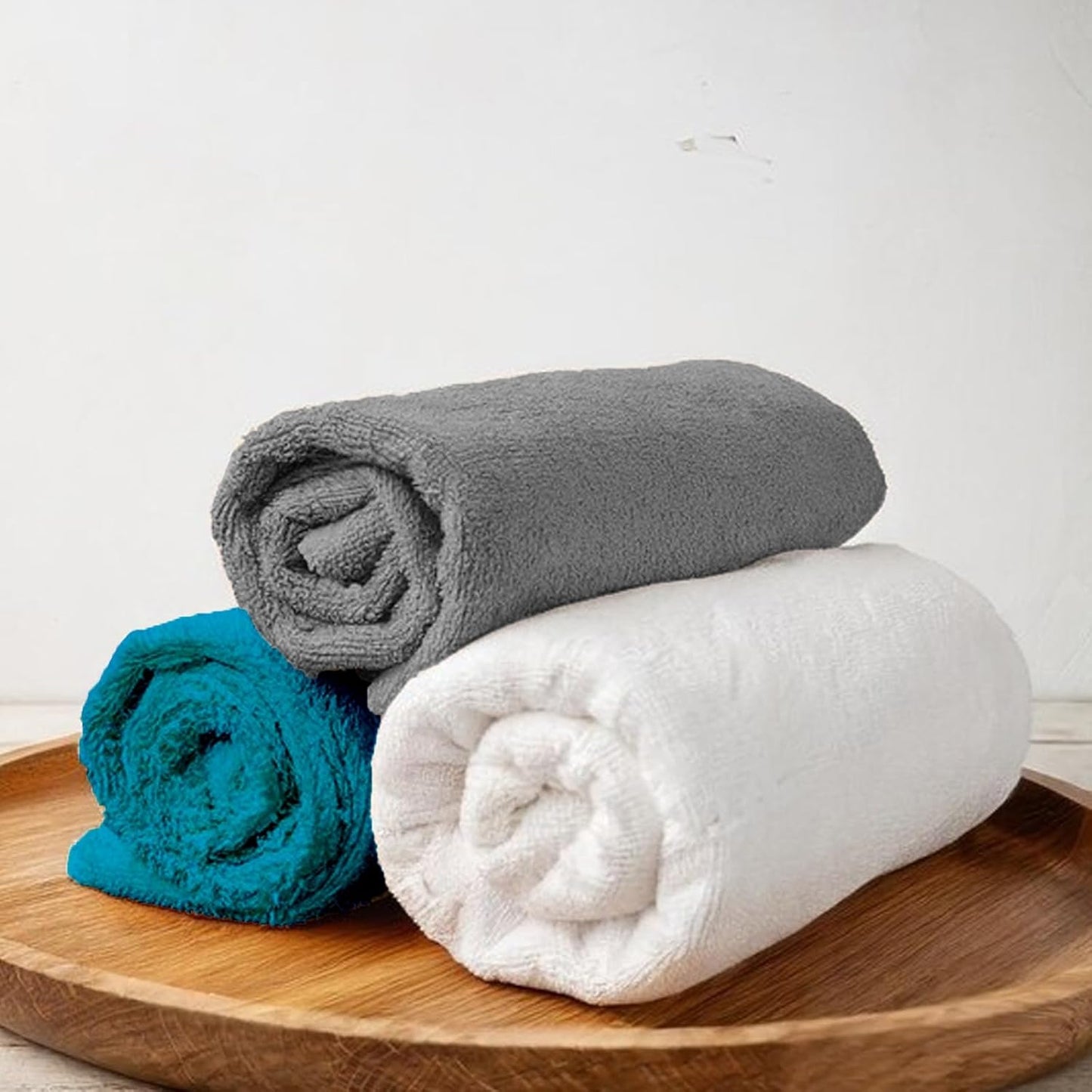 Stack of three rolled towels in gray, white, and blue placed on a wooden tray.