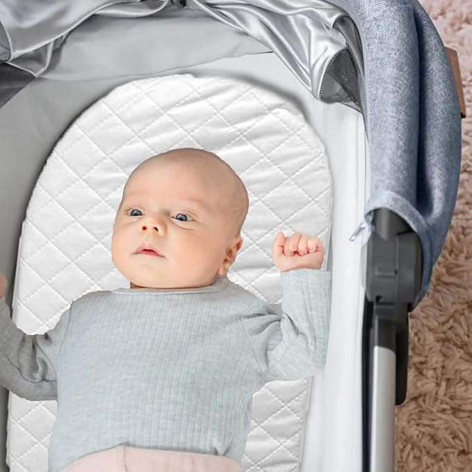 Baby lying on a white quilted mat inside a stroller with a gray cover.