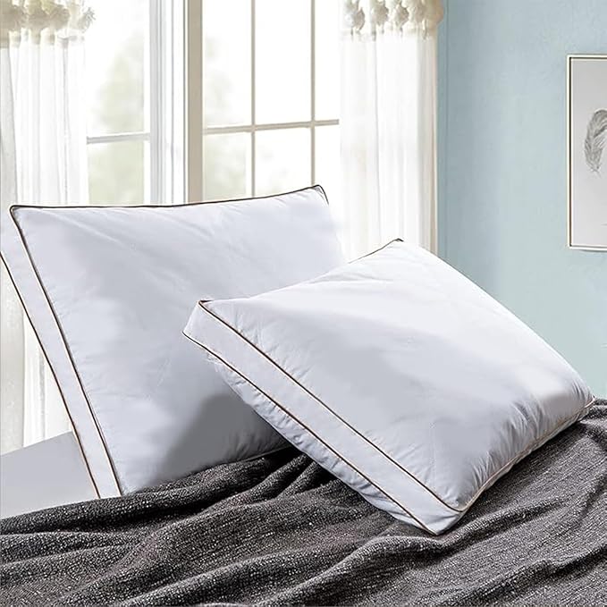 Two white pillows on a bed with a light blue wall and window in the background