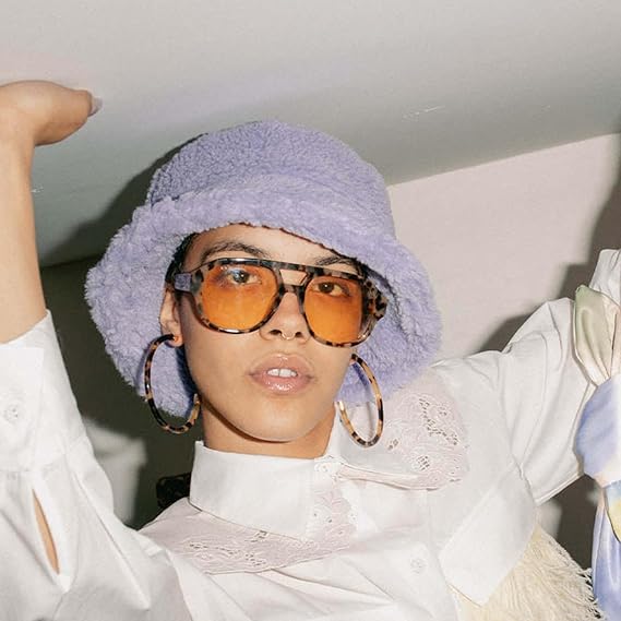 Person wearing a light purple bucket hat and orange-tinted glasses with a white lace shirt.