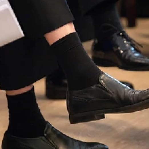 Close-up of black leather shoes and socks on a wooden floor.