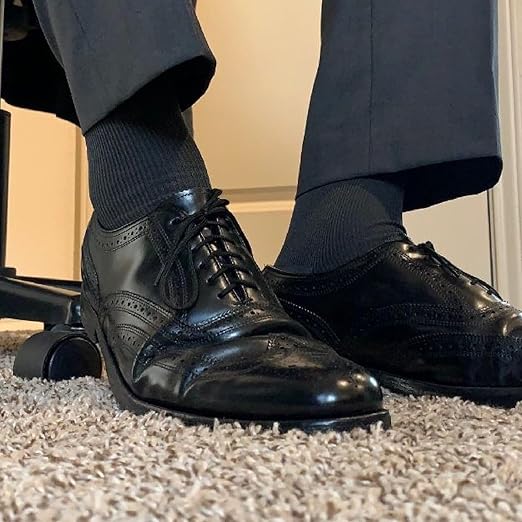 Black leather dress shoes worn with dark socks on a carpeted floor.