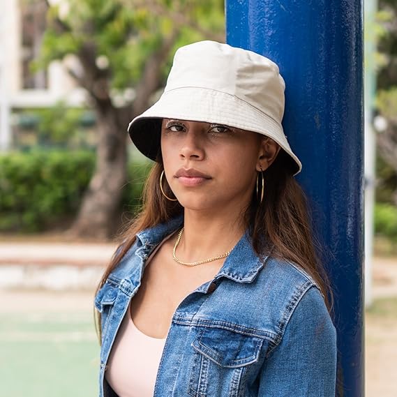 Woman wearing a beige bucket hat and denim jacket against a blue pole with greenery in the background