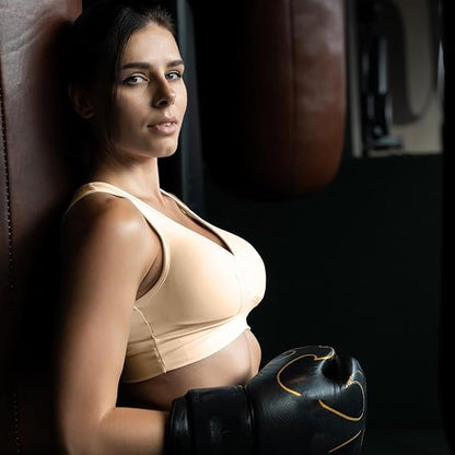 Woman in a sports bra and boxing gloves leaning against a punching bag.